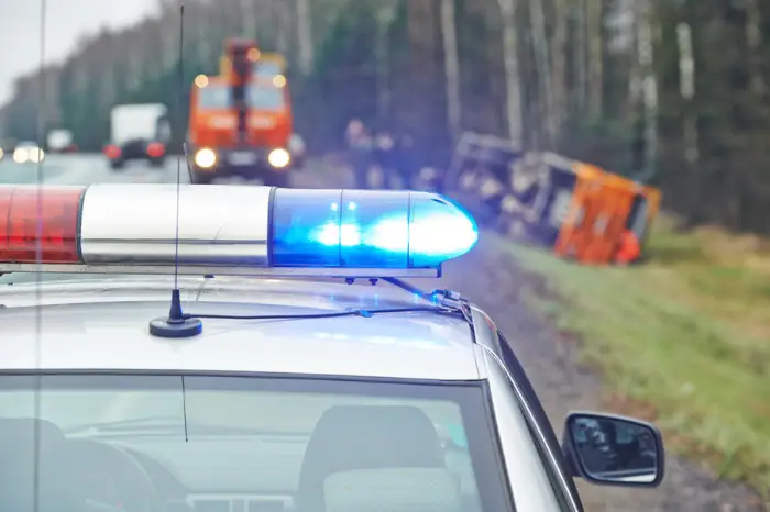 police car with a flasher in front of damaged lorry trailer in ditch of highway; Woman’s Sedan Struck by DPD Officer Received $145,000 Settlement