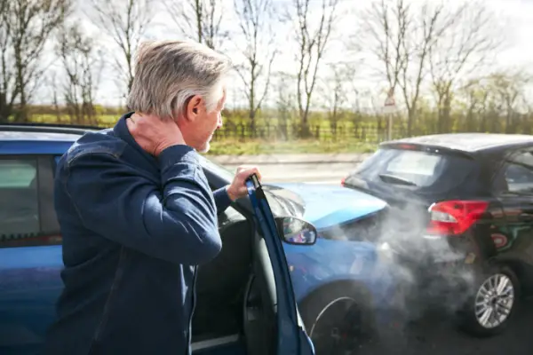 Senior male driver with whiplash injury getting out of car after traffic accident