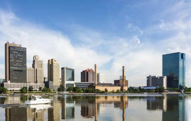 A panoramic view of downtown Toledo Ohio's skyline reflecting into the Maumee river with a power boat cruising by. A beautiful blue sky with white clouds for a backdrop.