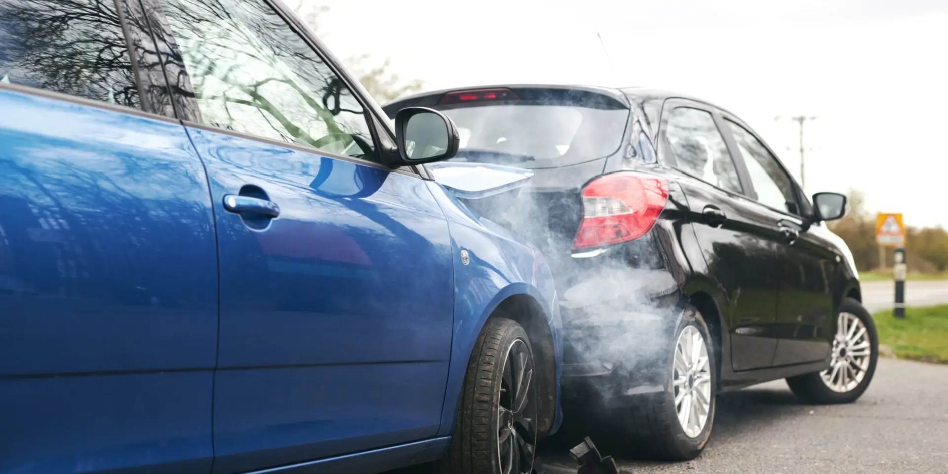 Two cars involved in traffic accident on side of the road with damage to bonnet and fender