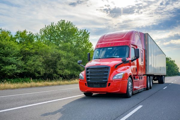 A red commercial truck driving on a two-lane highway.