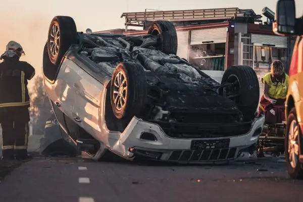 Horrific Traffic Accident Rollover Smoking and Burning Vehicle Lying on its Roof in the Middle of the Road after Collision. Daytime Crash Scene with Damaged Car.