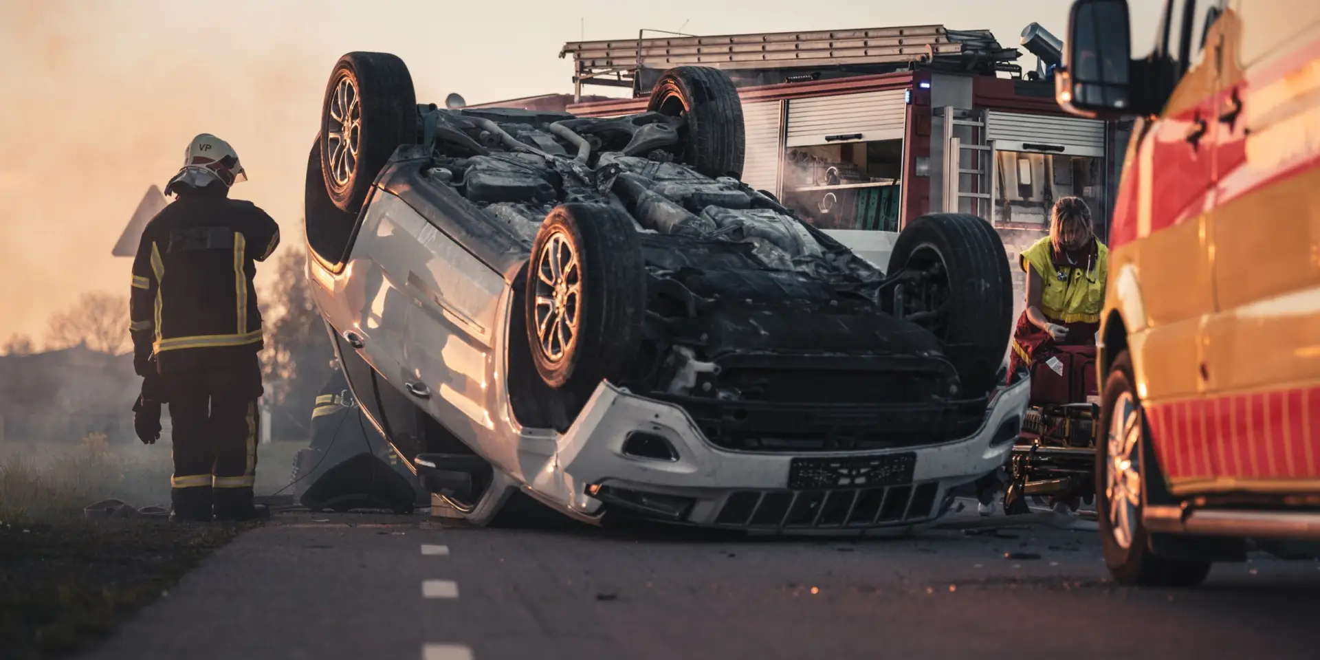 Horrific Traffic Accident Rollover Smoking and Burning Vehicle Lying on its Roof in the Middle of the Road after Collision. Daytime Crash Scene with Damaged Car.