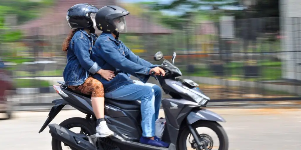 Yogyakarta Indonesia - 8 September 2024: photo of a black Honda Vario motorbike driver, middle-aged man riding with his wife, wearing a blue jacket and helmet, bokeh background, selective focus