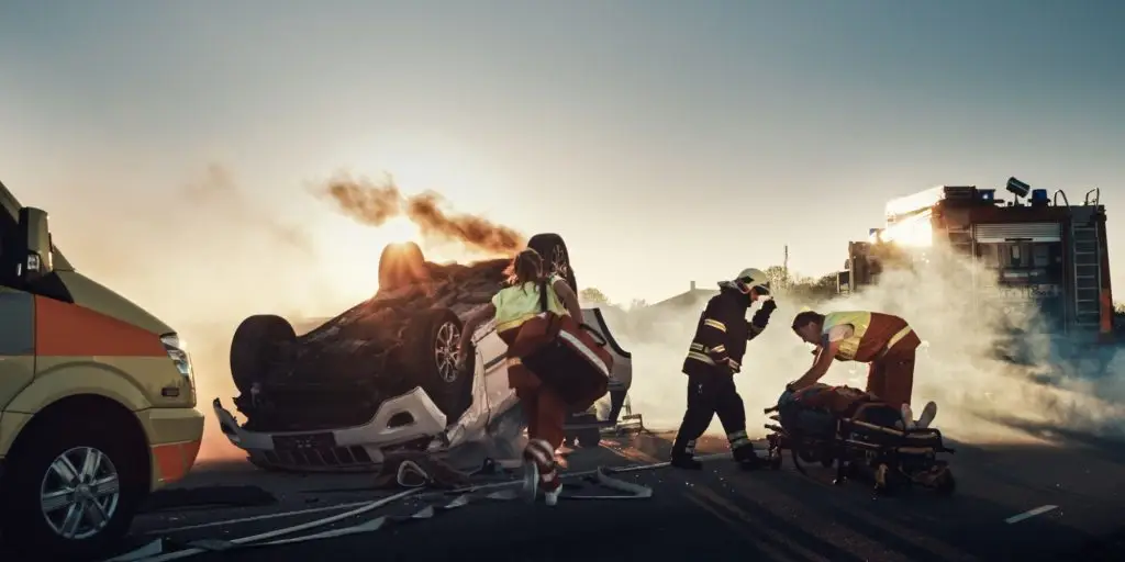 On the Car Crash Traffic Accident Scene: Rescue Team of Firefighters Pull Female Victim out of Rollover Vehicle, They Use Stretchers Carefully, Hand Her Over to Paramedics who Perform First Aid